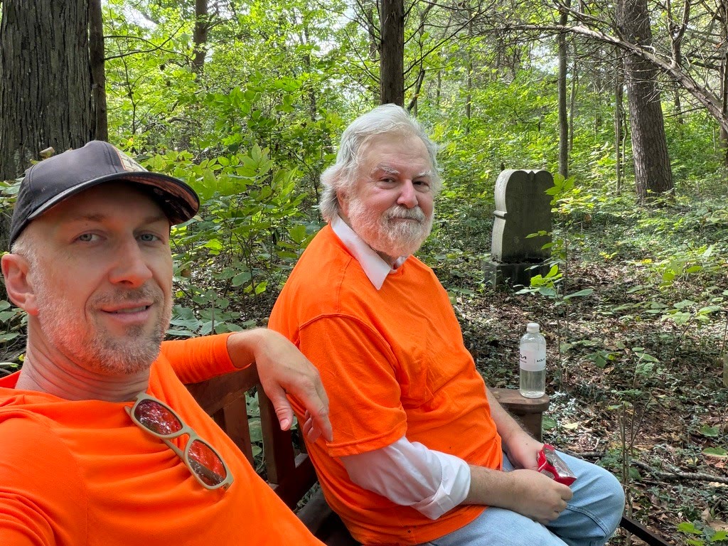 Josh and his dad in matching orange shirts, sitting on a bench in the woods