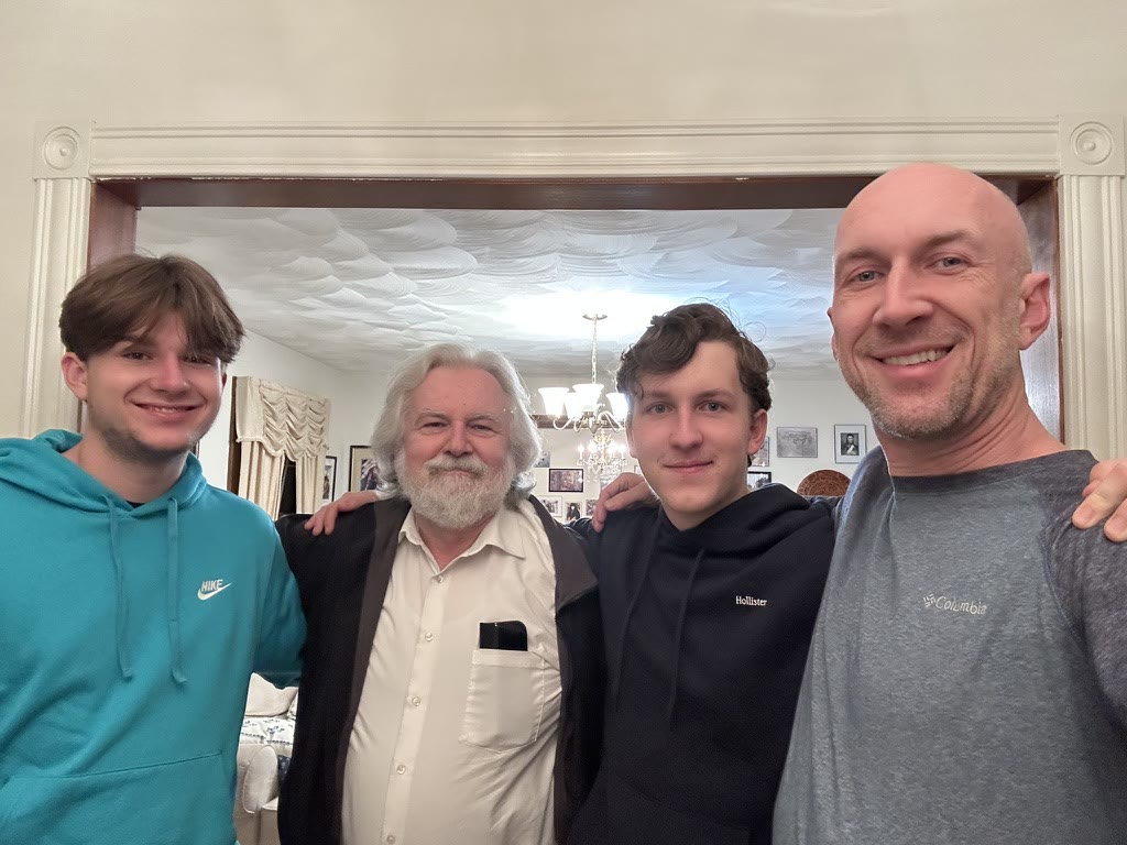 Josh, his dad, and Josh's two sons smiling together in his dad's living room
